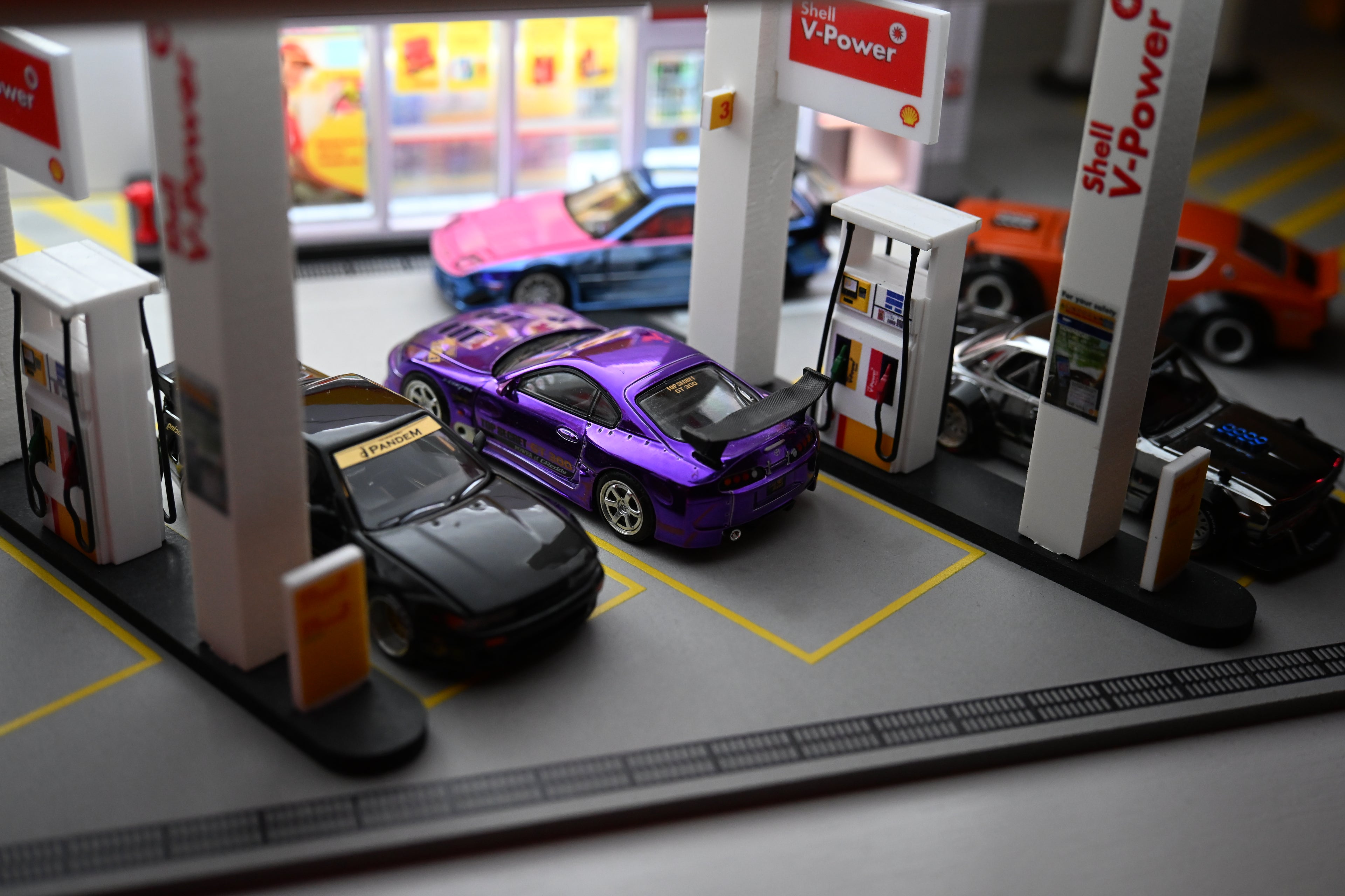 1:64 scale die-cast Top Secret Toyota Supra A80 in chrome purple displayed at a G-Fans Shell V-Power gas station diorama